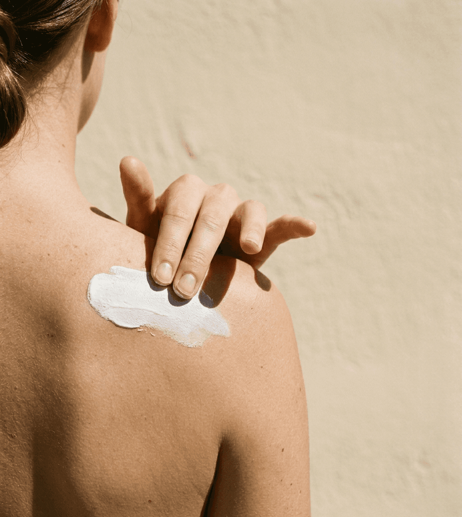 A hand smoothing balm into a bare shoulder in hard midday sunlight